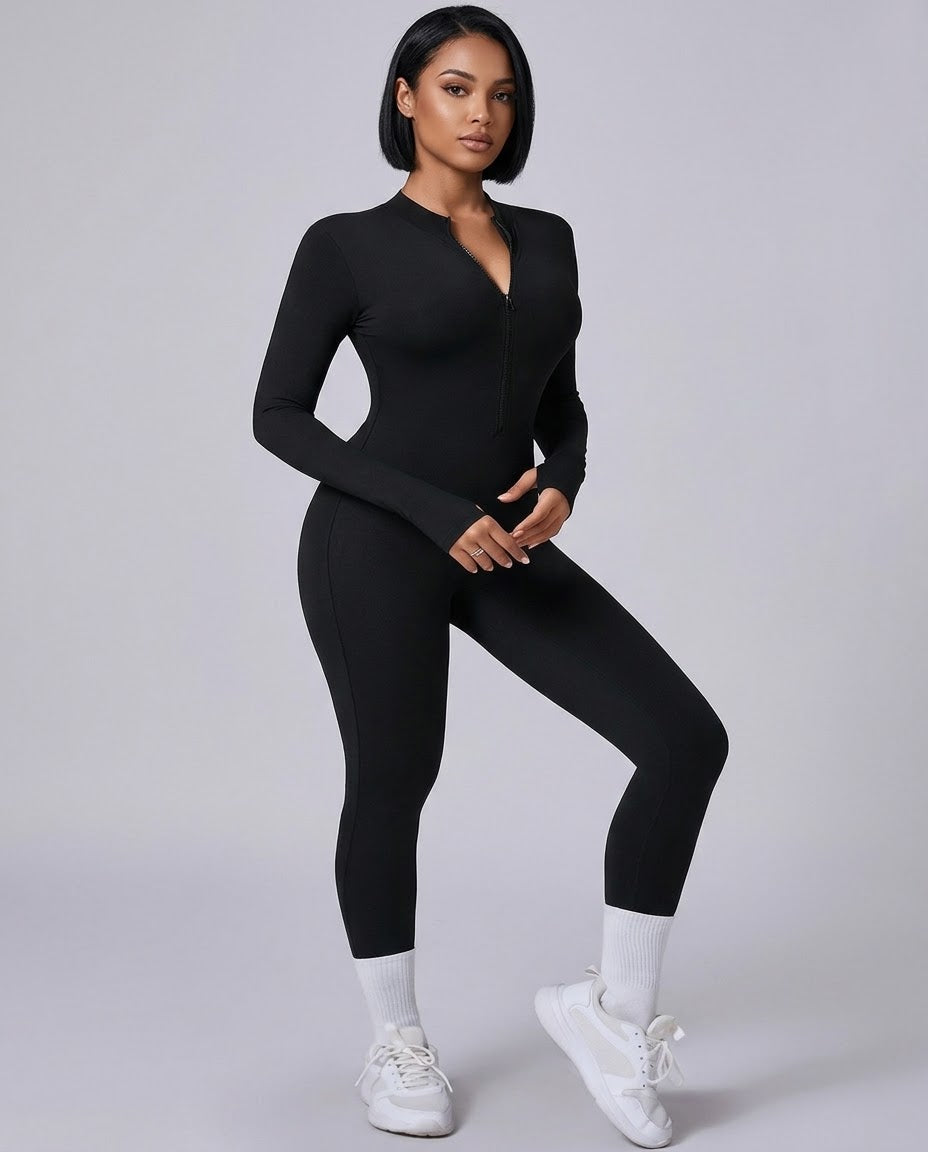 A woman modeling a black long-sleeve zip-up bodysuit with a deep V-neckline, paired with white socks and white sneakers, against a solid light gray studio background.
