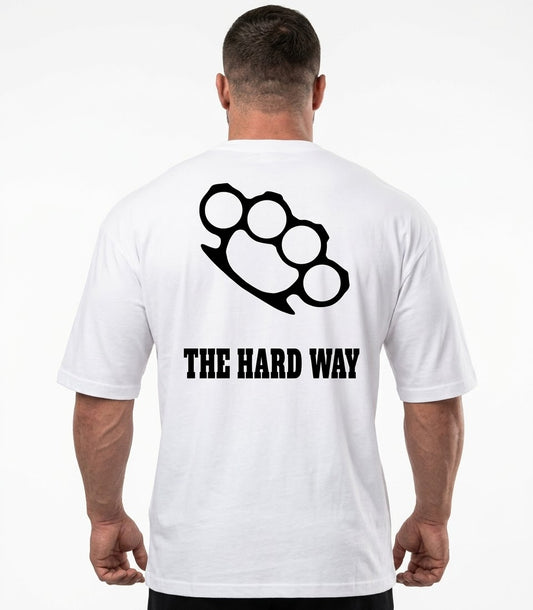 A man viewed from behind wearing a white t-shirt with a black brass knuckle graphic and the text 'THE HARD WAY' printed on the back.