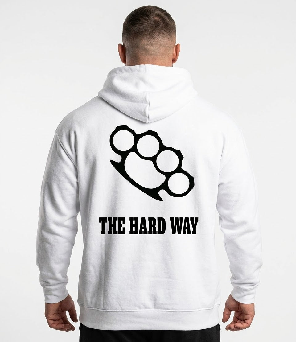 A man viewed from behind wearing a white hoodie with a black brass knuckle graphic and the text 'THE HARD WAY' printed on the back, against a plain white background.